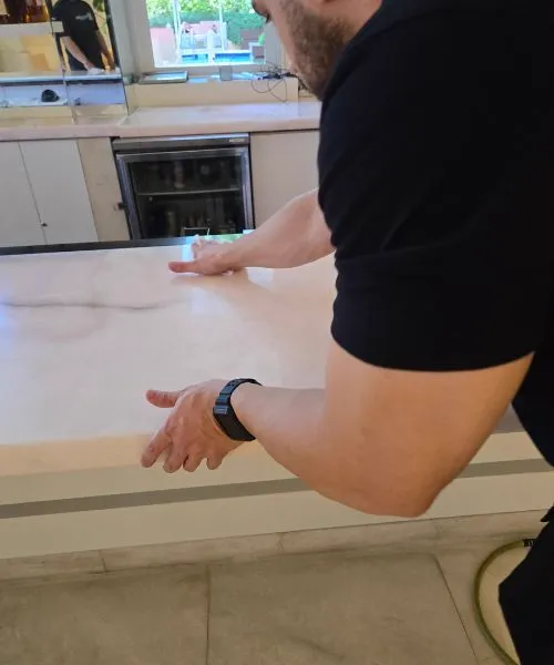 Close-up of an installer pressing down on a polished, light-colored marble or onyx countertop to apply or smooth an invisible protective film.