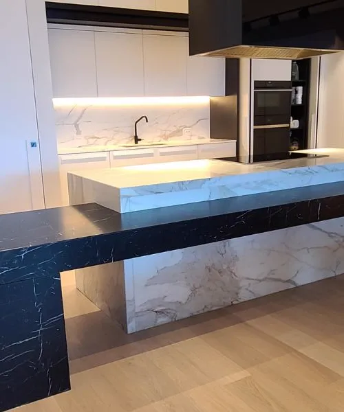 Detailed view of a contemporary kitchen island with black and white veined marble countertops, professionally protected. Background with white cabinets and black appliances.